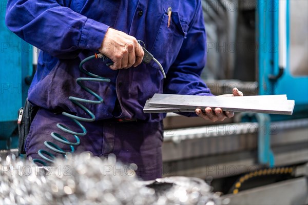 Factory worker operator in the numerical control sector cleaning a part with compressed air