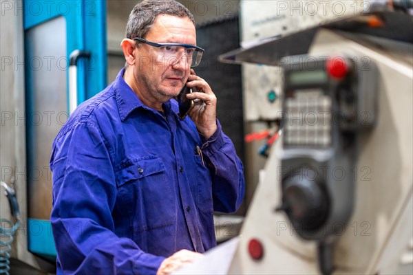 Factory worker operator in the numerical control sector talking on the phone with a client