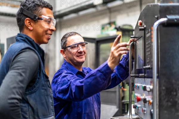 Instructor teaching the trade to a metal industrial factory worker in the numerical control sector