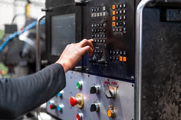 Unrecognizable operator touching the panel of a numerically controlled metal industrial factory machine