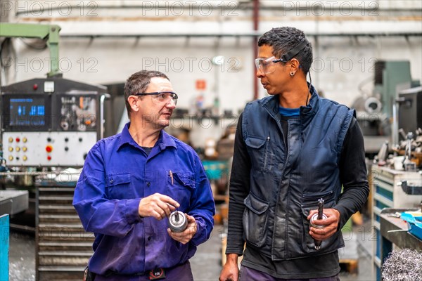 Instructor teaching and speaking the trade to a metal industrial factory worker in the numerical control sector