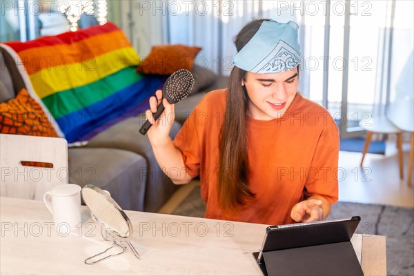 Transgender person brushing the long hair while using tablet sitting on the living room