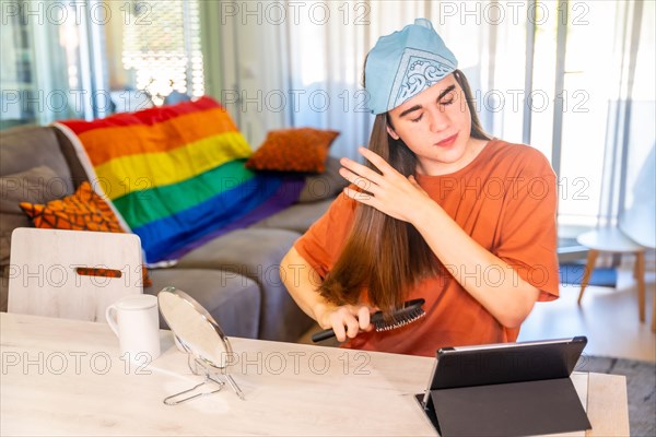 Gay man with long hair brushing it in the living room and using tablet