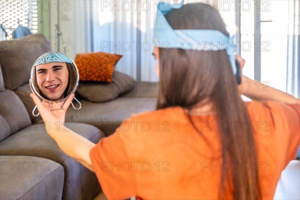 Groomed and freshly made up gay man gazes into a hand mirror at home