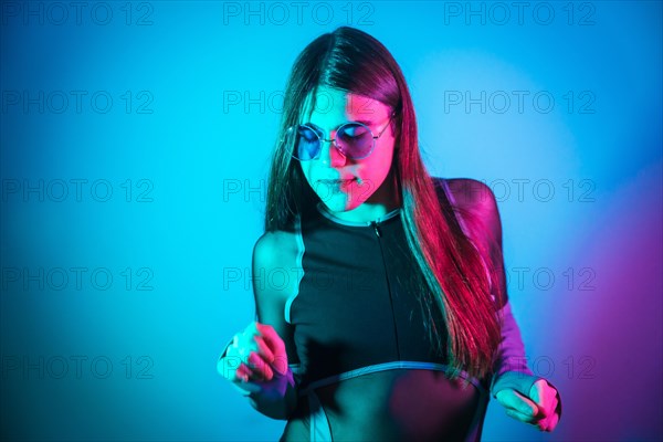 Sensual transgender person with long hair and sunglasses dancing in studio with neon lights