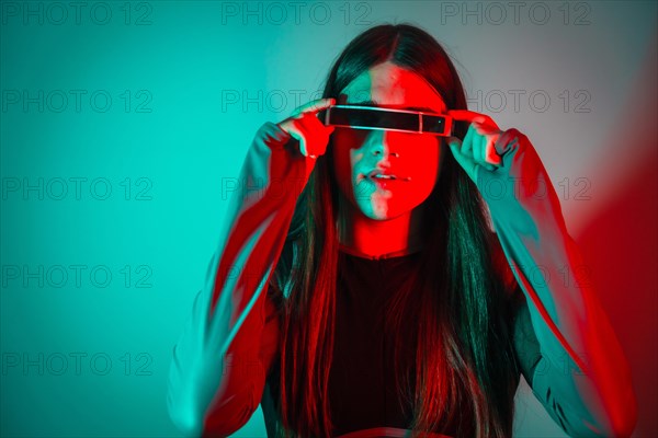 Futuristic studio portrait with neon lights of a transgender person with long hair using smart googles