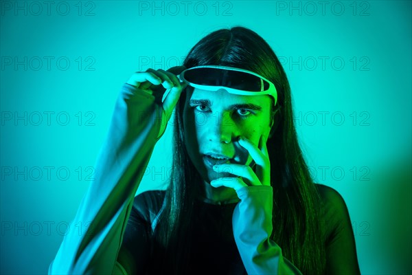 Studio portrait with neon lights of a surprised transgender non binary person using augmented reality futuristic goggles