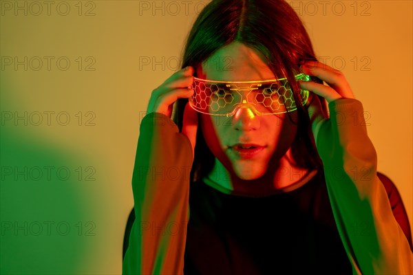 Futuristic studio portrait with neon lights of a transgender person looking at camera while using augmented reality goggles