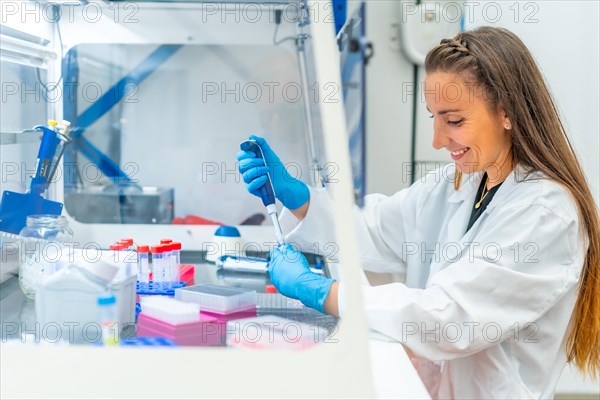 Smiling biologist using pipette to extract cells from a tray in a laboratory