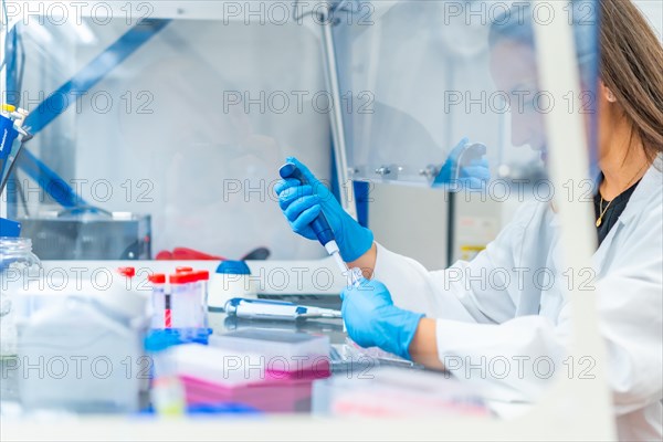 Woman working in a cancer research laboratory using a pipette to extract samples