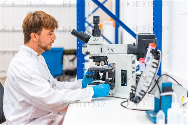 Side view of a young scientist using microscope to analyse samples in a cancer research laboratory