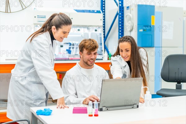 Smiling and proud young team of scientists using laptop in a research laboratory