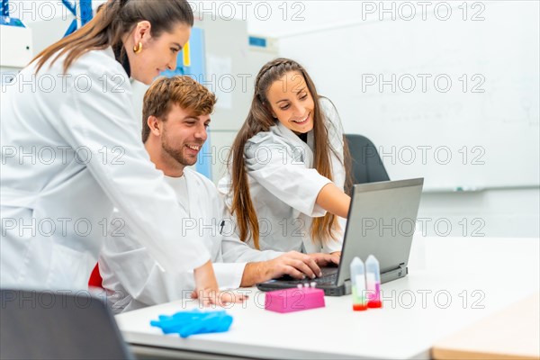 Scientist pointing the screen of a laptop next to colleagues in a research laboratory