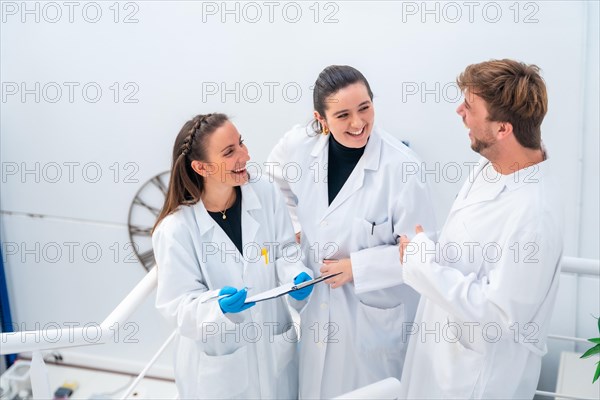 Side view and elevated view of three young scientists laughing while working in a cancer research laboratory