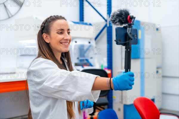 Side view of a friendly young scientist recording a tutorial online using mobile in a lab