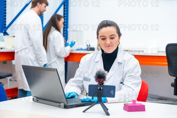 Young female scientist recording video with the mobile while using laptop in a research laboratory