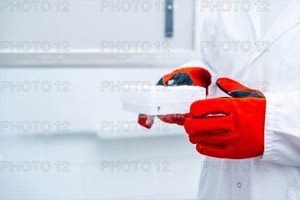 Close-up of a scientist with red gloves holding a box with frozen cells in an infectious disease prevention laboratory