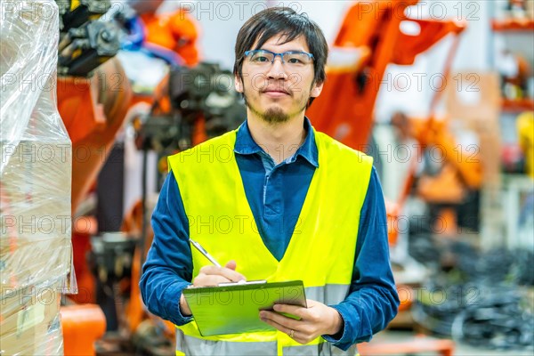 Japanese engineer preparing production reports in an assembly line of industrial robotic arms