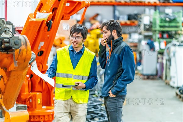 Software engineer explaining to controlling robotic welding process to welder in factory