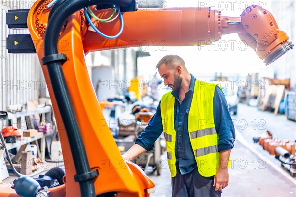 Young worker uses a paintbrush to paint an industrial robotic arm