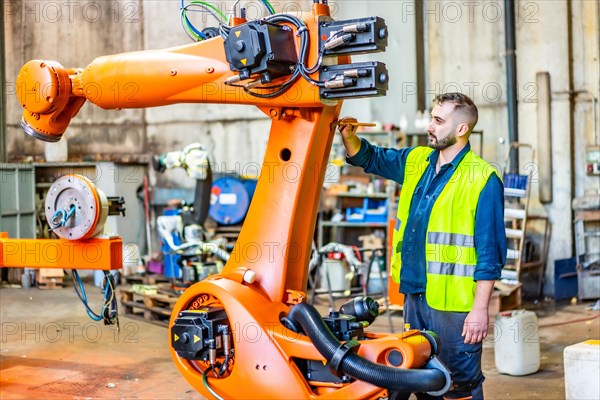 Young worker uses a paintbrush to paint details of an industrial robotic arm