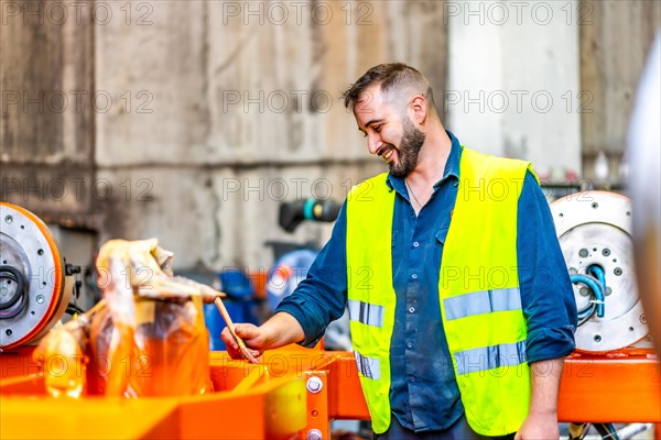 Happy worker painting a part of a robotic arm indoors in a industry