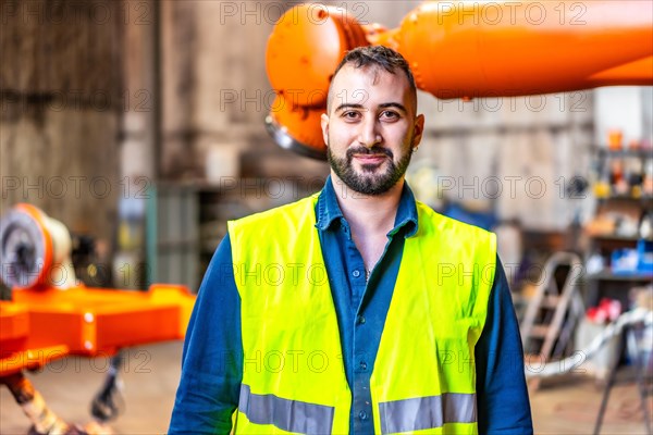 Close-up portrait of a smiling mechanic in a factory of robotic arms