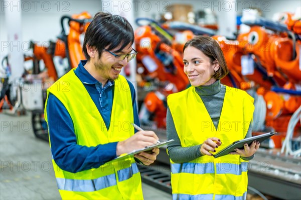 Multicultural male and female engineers smiling while controlling the assembly line of a robotic arms factory