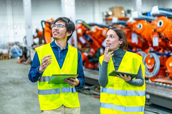 Japanese and caucasian engineers reporting in line of industrial robotic arms