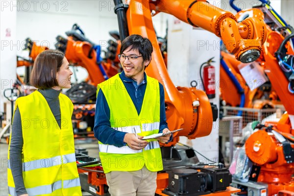 Distracted multi-ethnic engineers walking next to a robotic arms assembly line in a factory