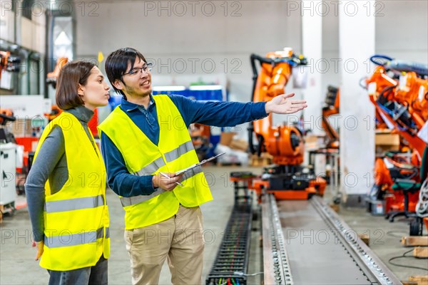 Side view photo of a japanese chief engineer explaining to controlling robotic welding process to a caucasian women