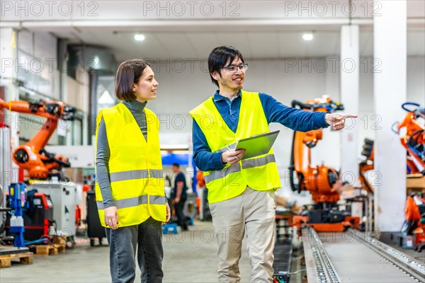 Japanese chief engineer explaining and pointing robotic welding process to a caucasian women in a factory