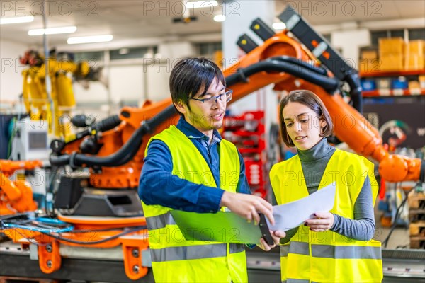 Multicultural engineers doing paperwork in an assembly line of robotic arms production