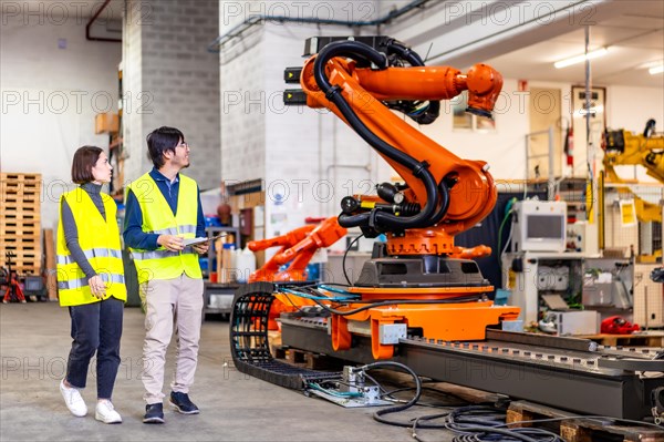 Two multi-ethnic engineers walking into the factory of robotic arms production