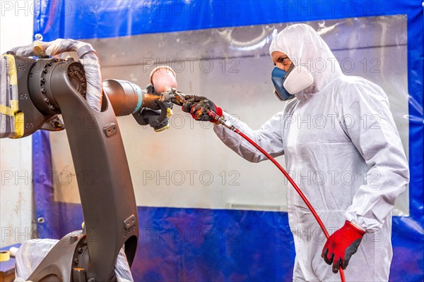 Industrial painter using a spray gun to paint a robotic arm in an industrial robot industry