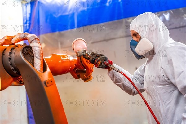 Painter with protective gear using a spray gun to paint an industrial robot arm in a factory
