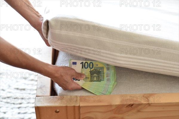 A hand deposits many hundred euro banknotes under a mattress