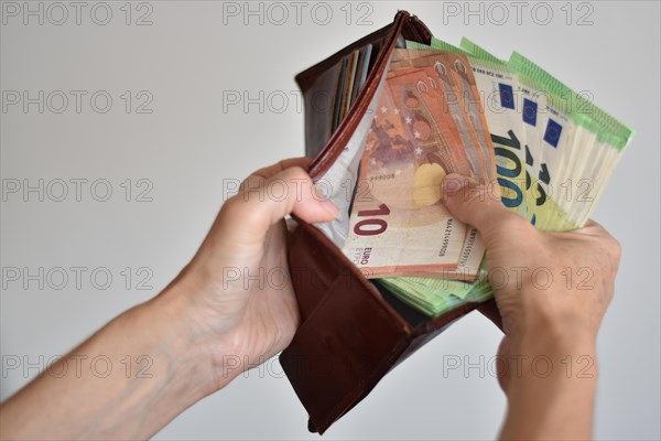 Hands holding many euro banknotes in a leather wallet