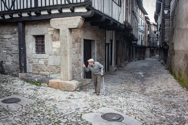 Old man with crutch and walking stick in an alley in La Alberca