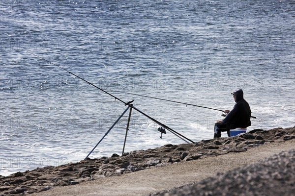 Angler fishing at sea from dyke