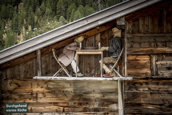 Funny scene on wooden alpine barn showing two straw figures drinking beer at a table