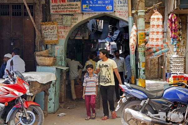 Pedestrians shopping in busy alley with stores selling goods on the street in Old Delhi