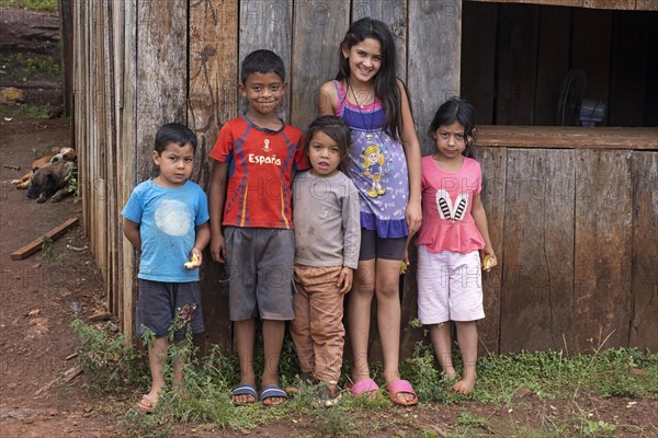 Paraguayan children posing in front of primitive wooden house in the town Edelira in rural Itapua