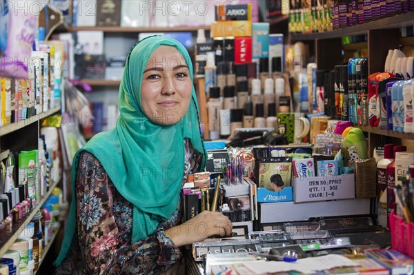 Young Kyrgyz woman with head scarf selling cosmetics in drugstore in the city Osh