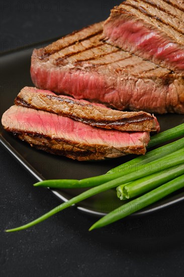 Closeup view of grilled tri-tip loin beef steaks medium rare with fresh vegetables on black background