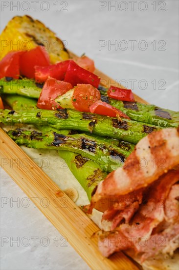 Grilled asparagus with bacon and corn on wooden serving board