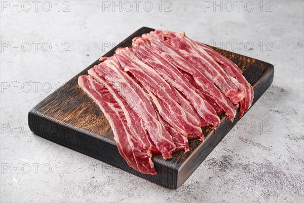 Fresh raw beef bacon strips on wooden cutting board