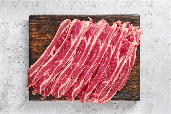 Top view of wooden cutting board with fresh raw beef bacon strips