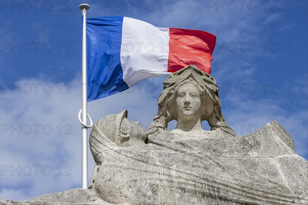 Detail of the First World War stone monument Monument aux Morts with the French flag behind it