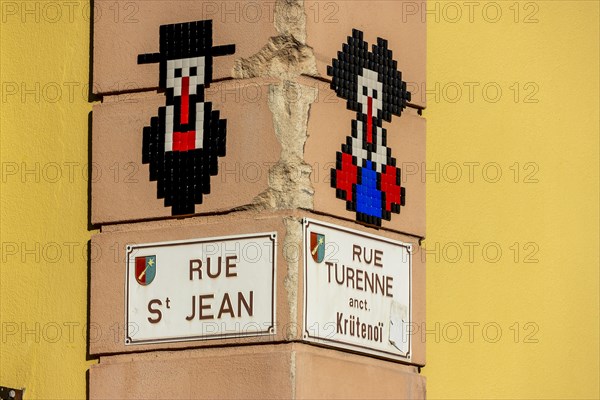 Corner of a building with street name plaques and a mosaic of a man and a woman